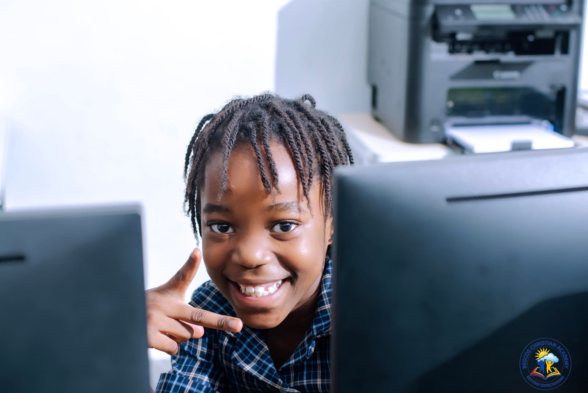 A pupil smiling beside a computer monitor in the ICT lab