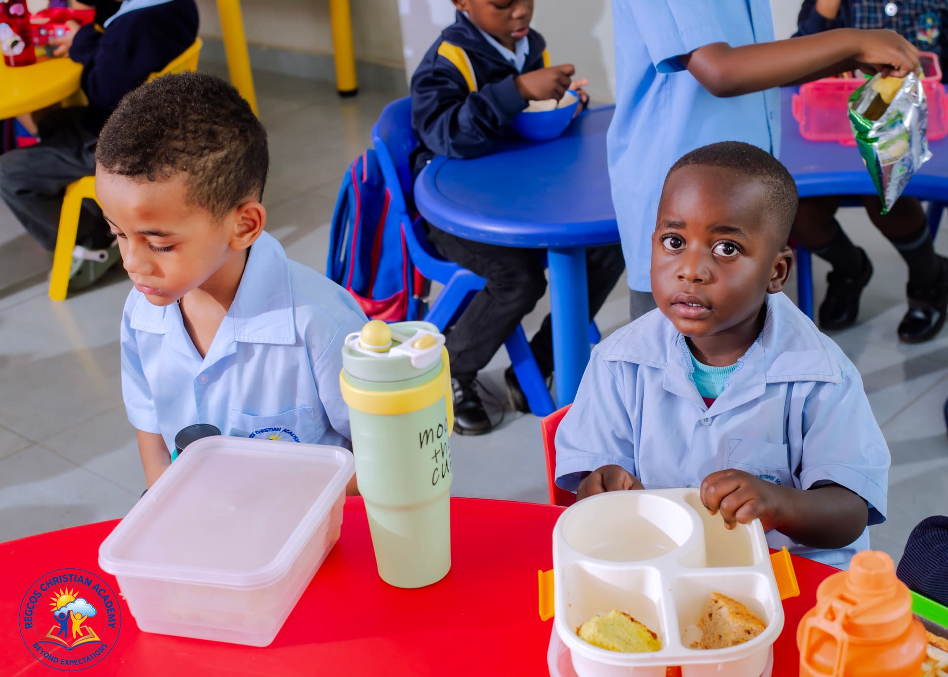 Two young pupils with their lunch boxes at a preschool table